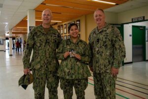 Navy personnel pose together, one holding an award, in a military office.