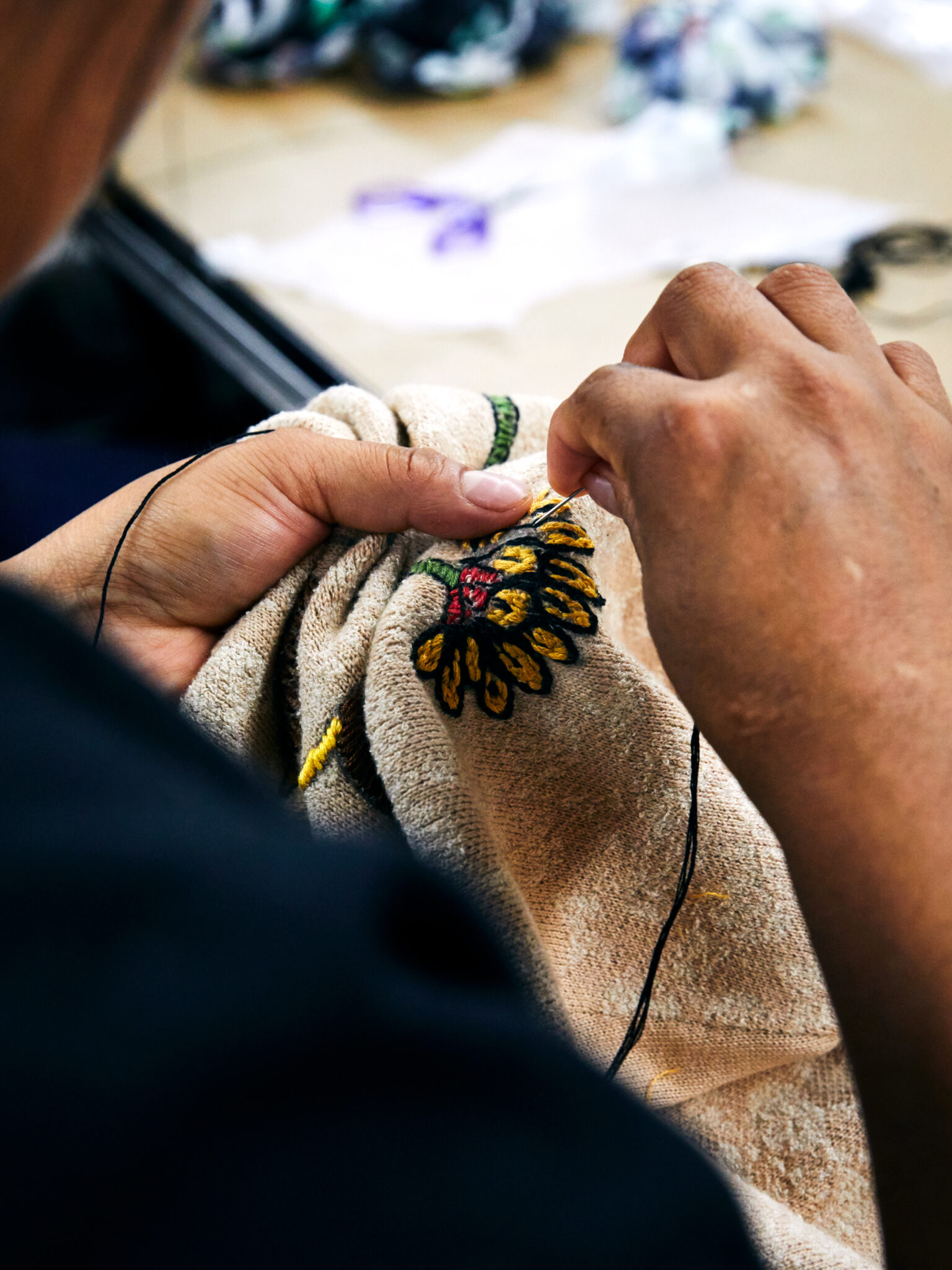 Close-up of artisan hands stitching floral embroidery on soft beige velvet fabric.