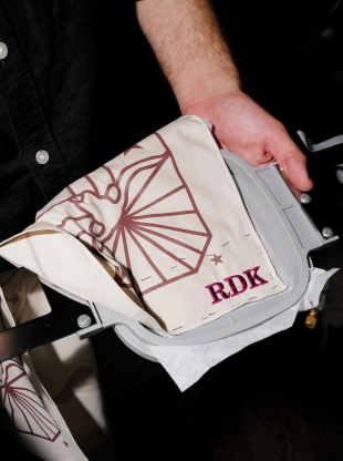Close-up of hands holding embroidered tote bag with “RDK” and star patterns.