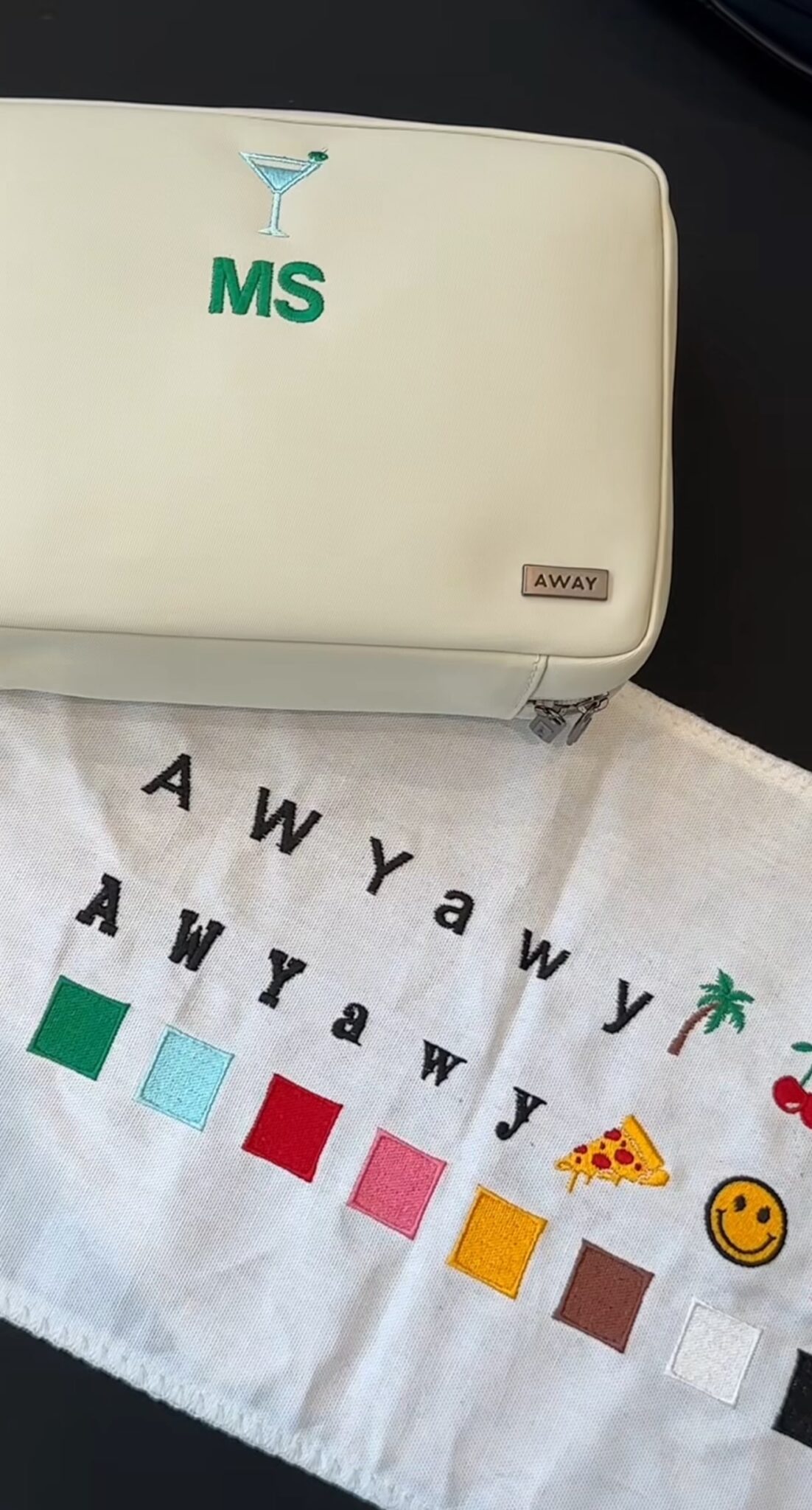 Fabric swatch with repeated “AWyawy” logos, color blocks, and icons beside a suitcase.