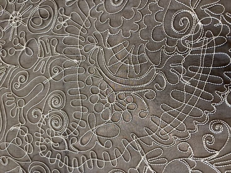 Intricate swirling quilting lines on taupe fabric using free-motion stitching.