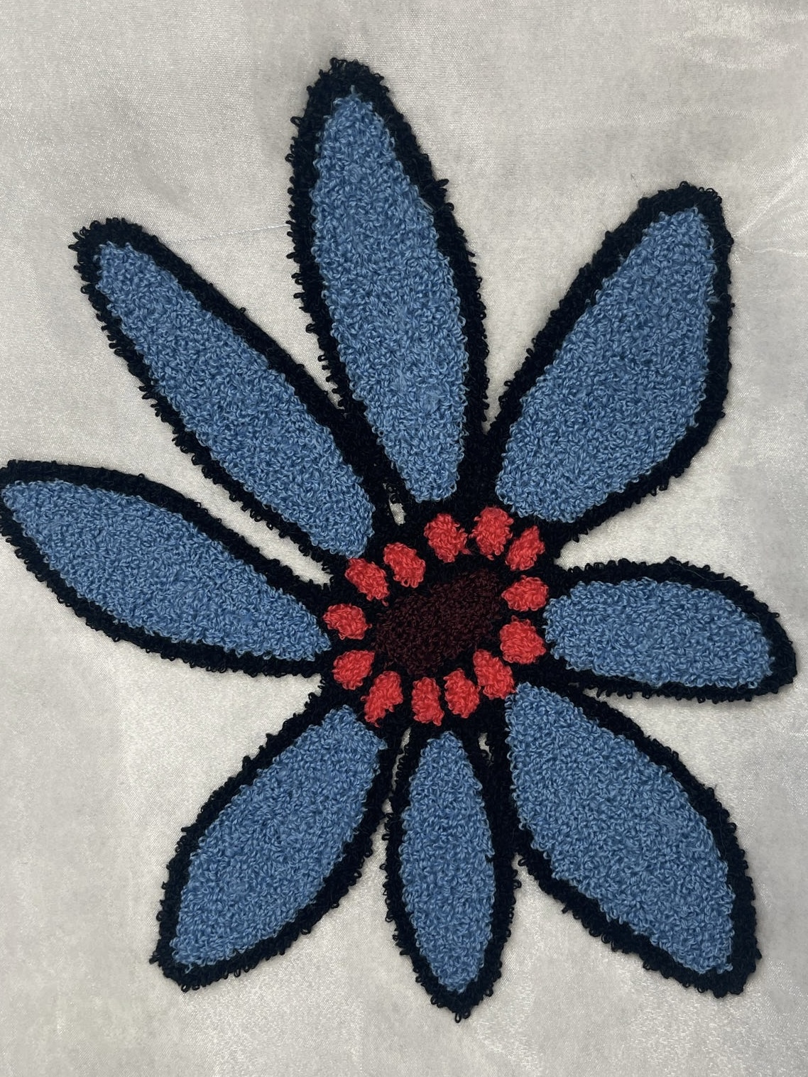 Blue chenille flower tufted on white textile with red accents.