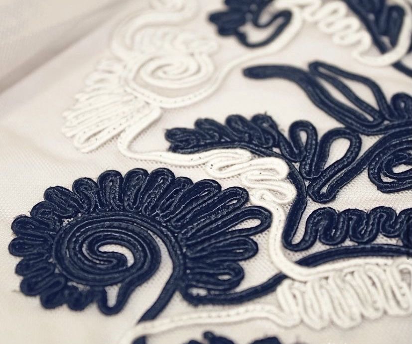 White fabric embroidered with thick navy cords in abstract floral shapes.