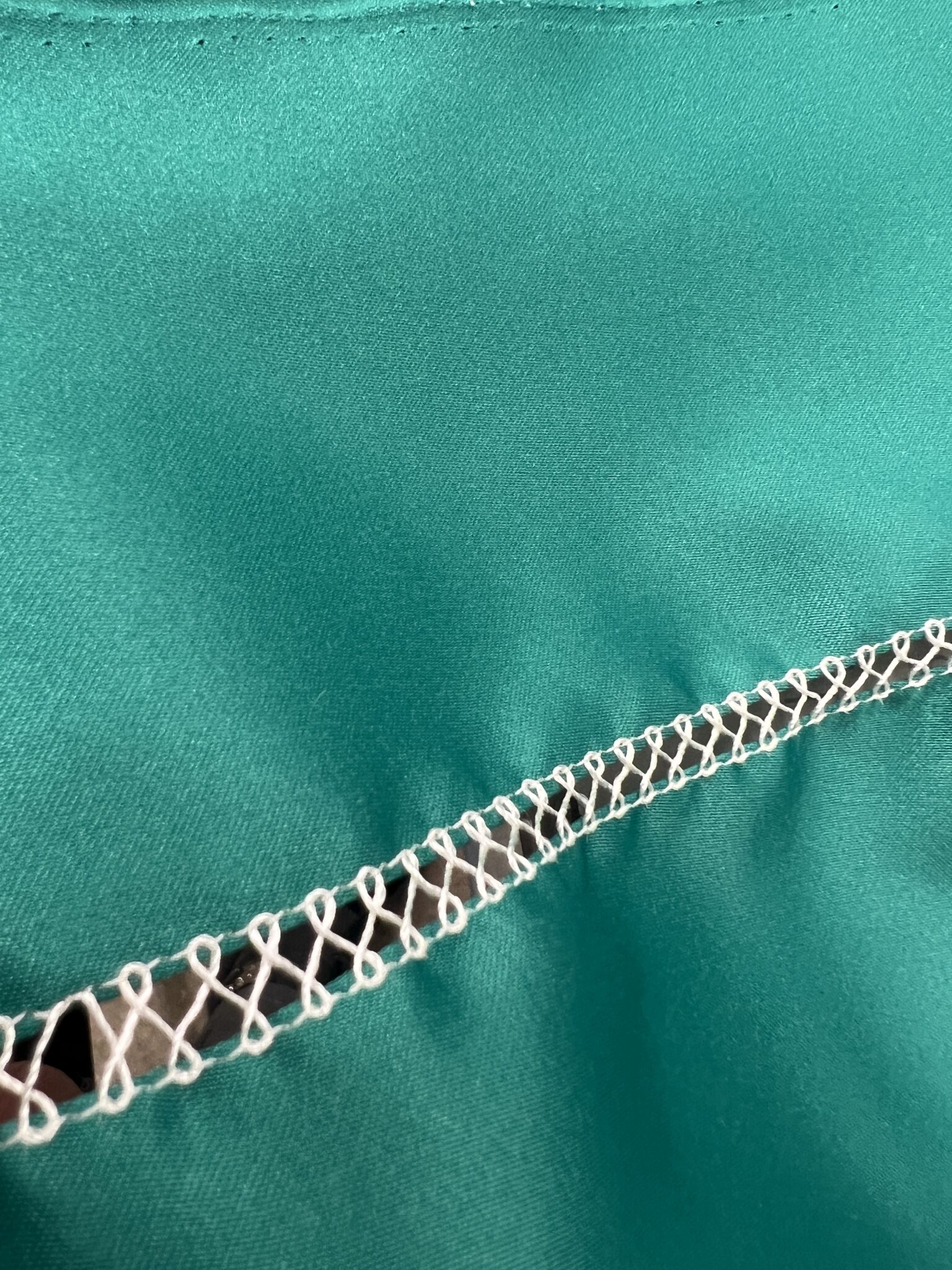 Industrial-style white coverstitch detail on vibrant teal fabric.