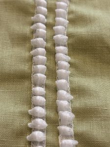 Close-up of white 3D rolled cords stitched onto yellow fabric.