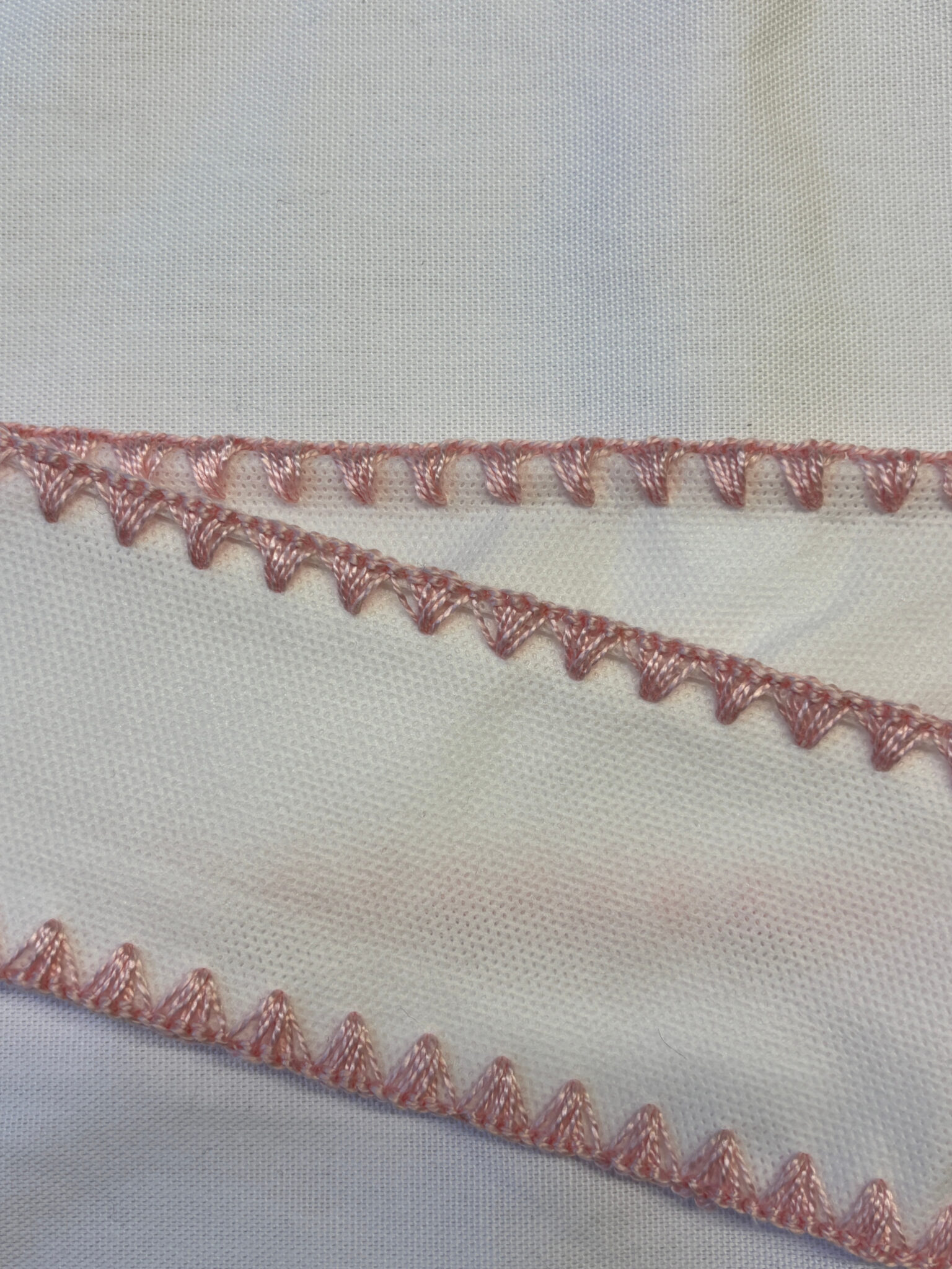 Decorative overlock stitching in pink thread on white base.