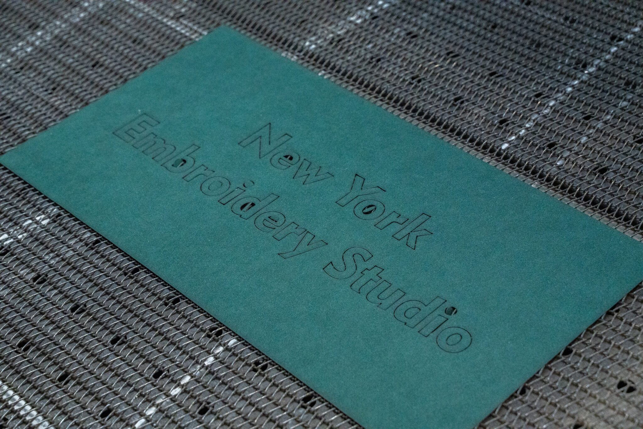 Green textured card with “New York Embroidery Studio” embossed on it.