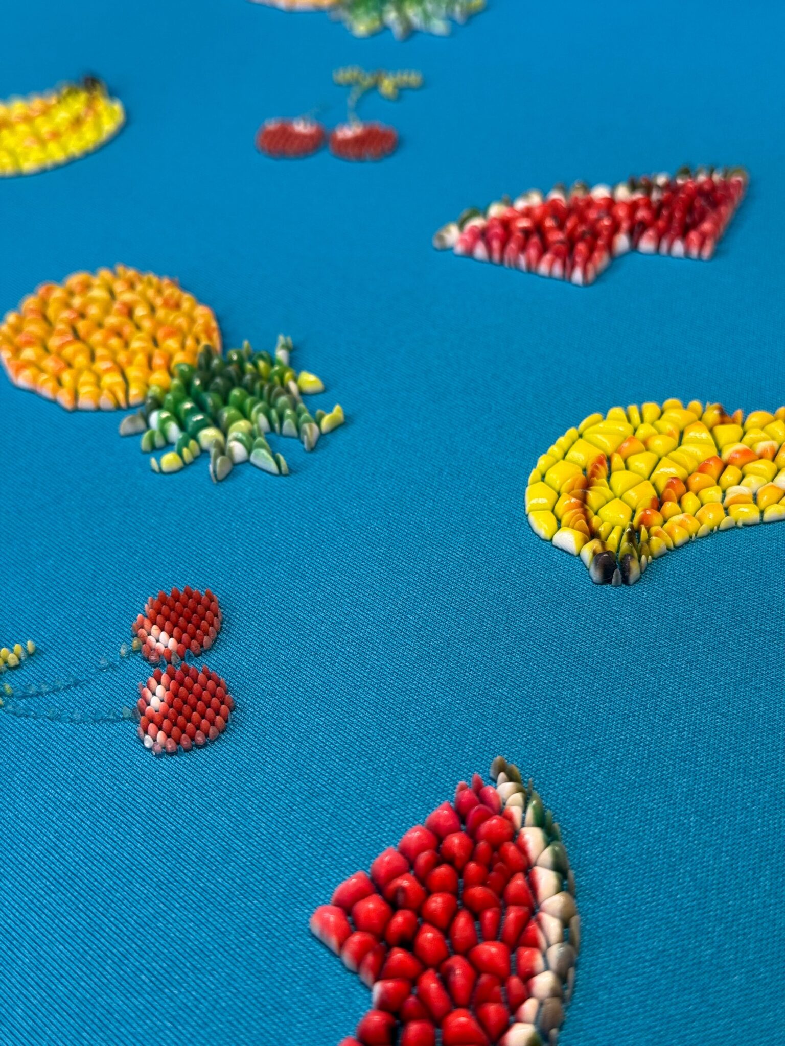 Beaded fruits like cherries and pineapples embroidered on bright blue fabric.