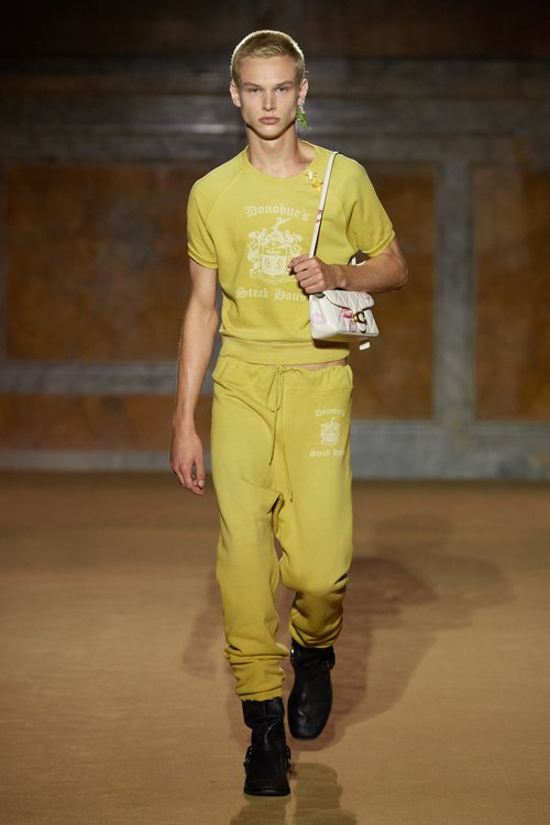 Model in a monochromatic yellow sporty knit set featuring a short-sleeve top and jogger-style pants, accessorized with a small white shoulder bag.