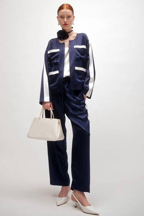 Woman wearing a navy blue and white color-blocked pantsuit with wide-leg trousers and a matching cropped jacket, holding a light beige handbag.