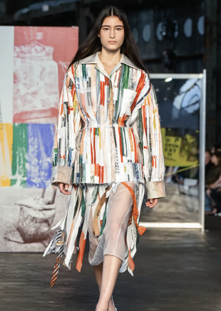 Runway shot of a model wearing Jason Wu SS26 patchwork collage dress, featuring bias-cut strips of silk and novelty fabrics in custom colorways, with raw-edge satin and sheer organza details.