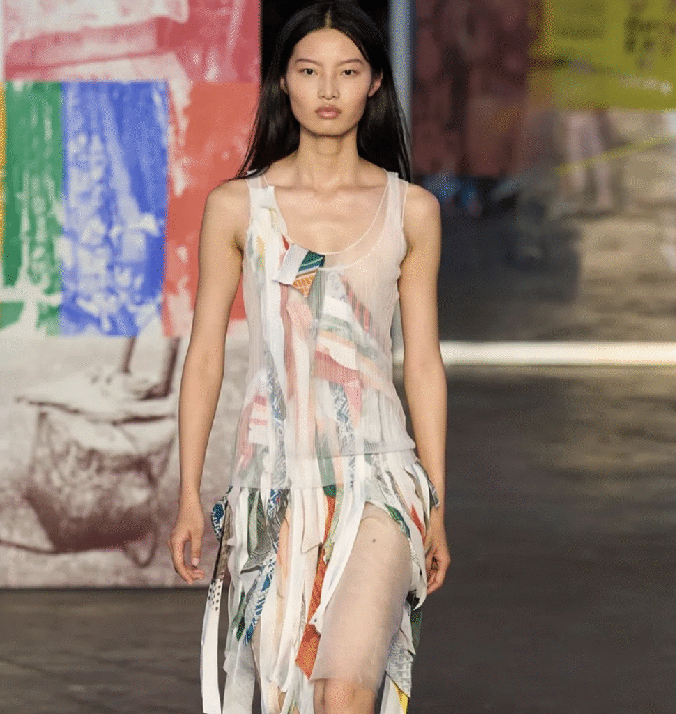 Runway shot of a model wearing Jason Wu SS26 patchwork collage dress, featuring bias-cut strips of silk and novelty fabrics in custom colorways, with raw-edge satin and sheer organza details.
