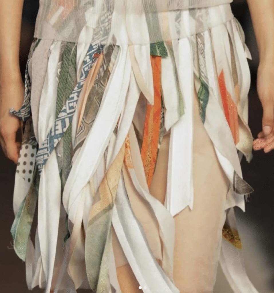 Runway shot of a model wearing Jason Wu SS26 patchwork collage dress, featuring bias-cut strips of silk and novelty fabrics in custom colorways, with raw-edge satin and sheer organza details.