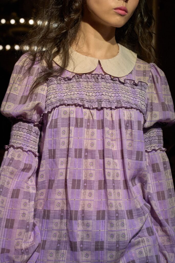Runway shot of a model wearing an Anna Sui SS26 look featuring delicate shirring and hand-applied embellishments, creating a romantic, textured silhouette.