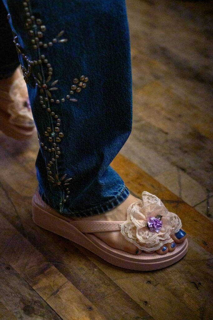 Runway shot of a model wearing an Anna Sui SS26 look featuring delicate shirring and hand-applied embellishments, creating a romantic, textured silhouette.