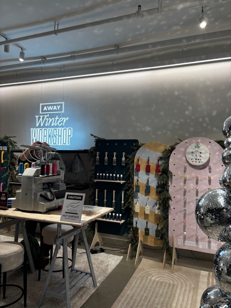 New York Embroidery Studio’s on-site embroidery machine, thread displays, and customization station inside AWAY’s Winter Workshop holiday pop-up.