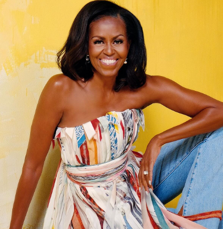 Michelle Obama standing against a textured yellow wall wearing a multicolored ribbon-strip top with long flowing ties and denim pants in an editorial portrait for People magazine.