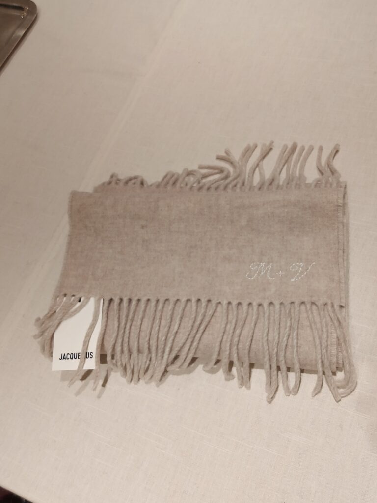 Hand-embroidered white initials stitched onto a beige cashmere scarf with hand-tied fringe detailing