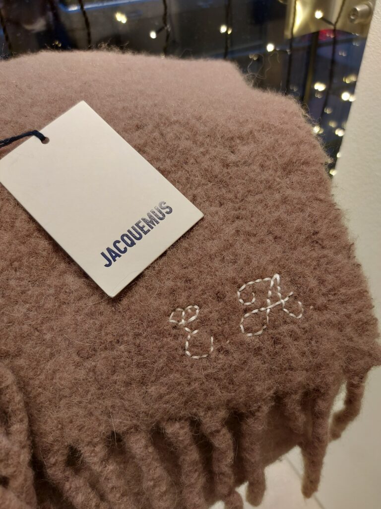 Hand-embroidered white initials stitched onto a beige cashmere scarf with hand-tied fringe detailing