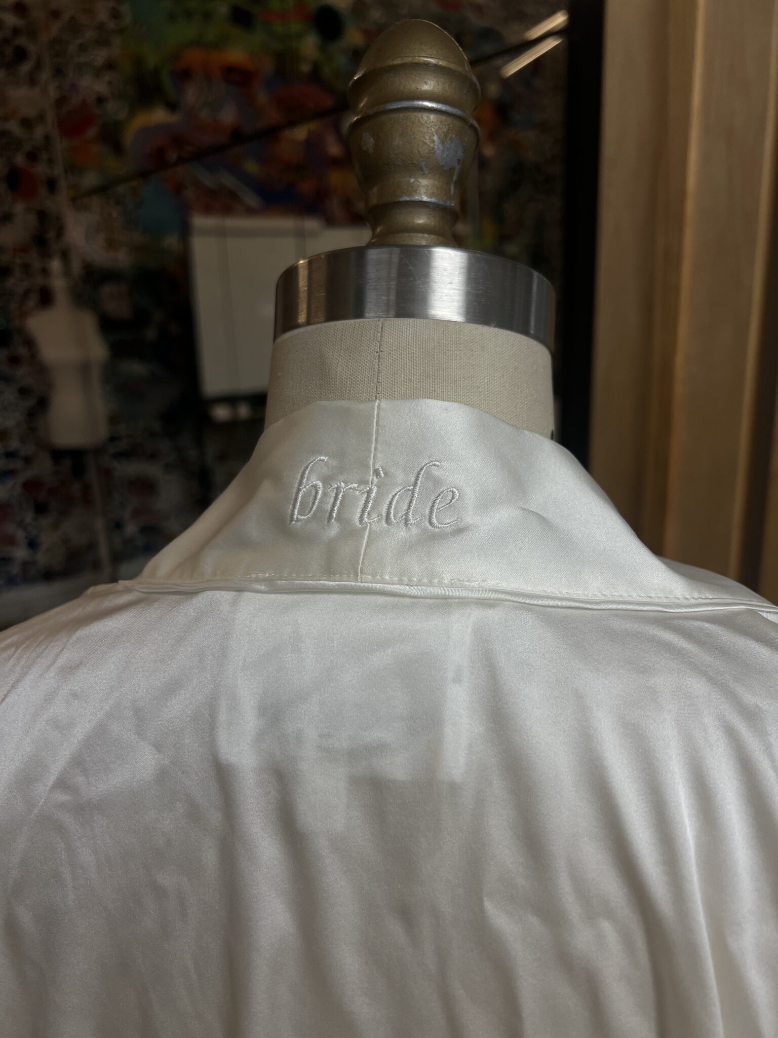 White bridal garment on a dress form with “bride” embroidered on the back of the collar