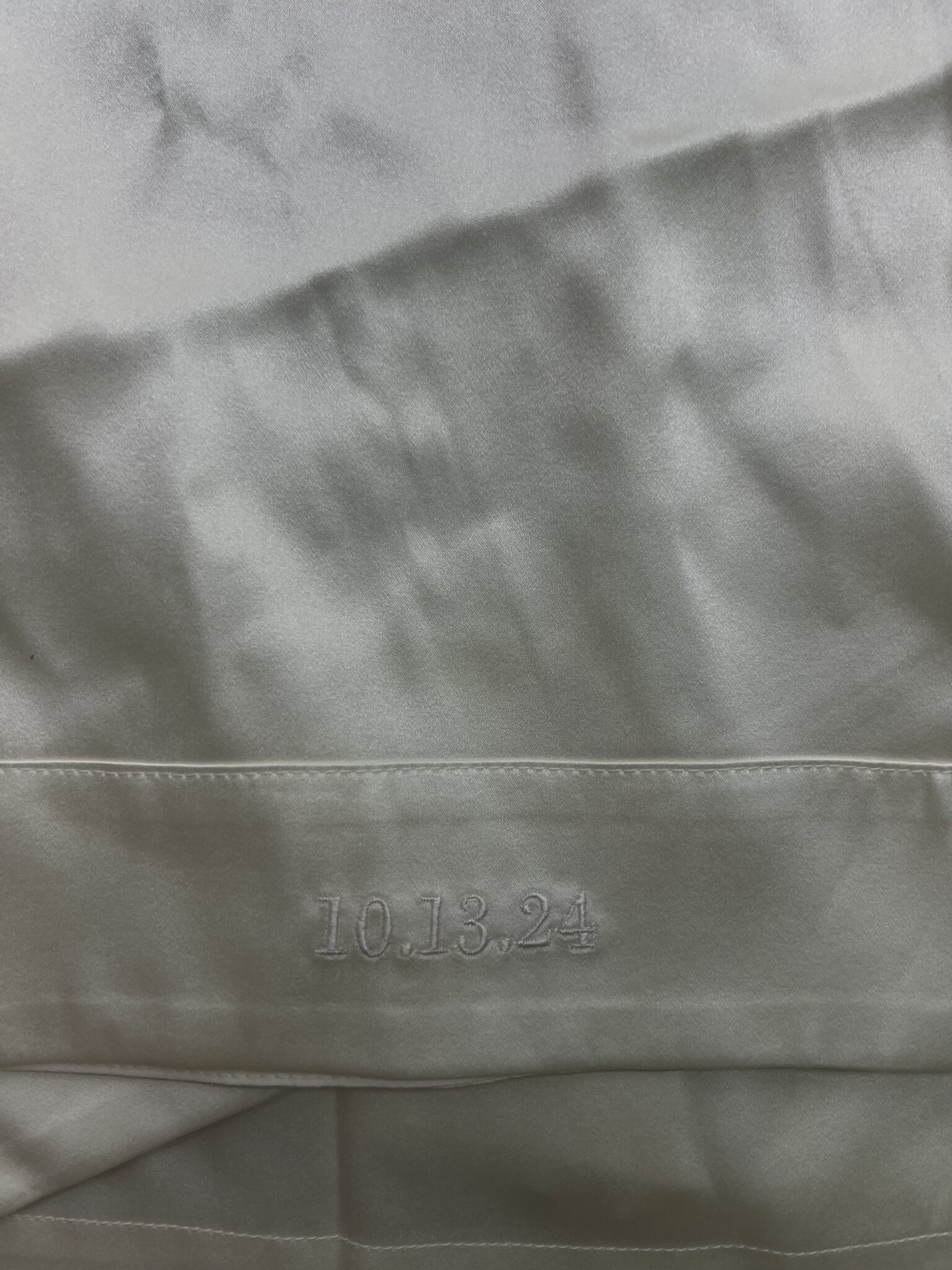 Close-up of white embroidered wedding date “10.13.24” on a bridal garment