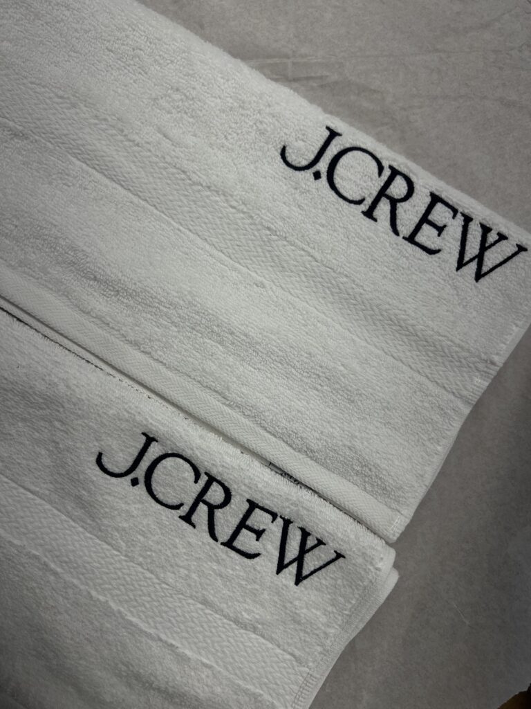 Angled view of white towels featuring black embroidered J.Crew logos