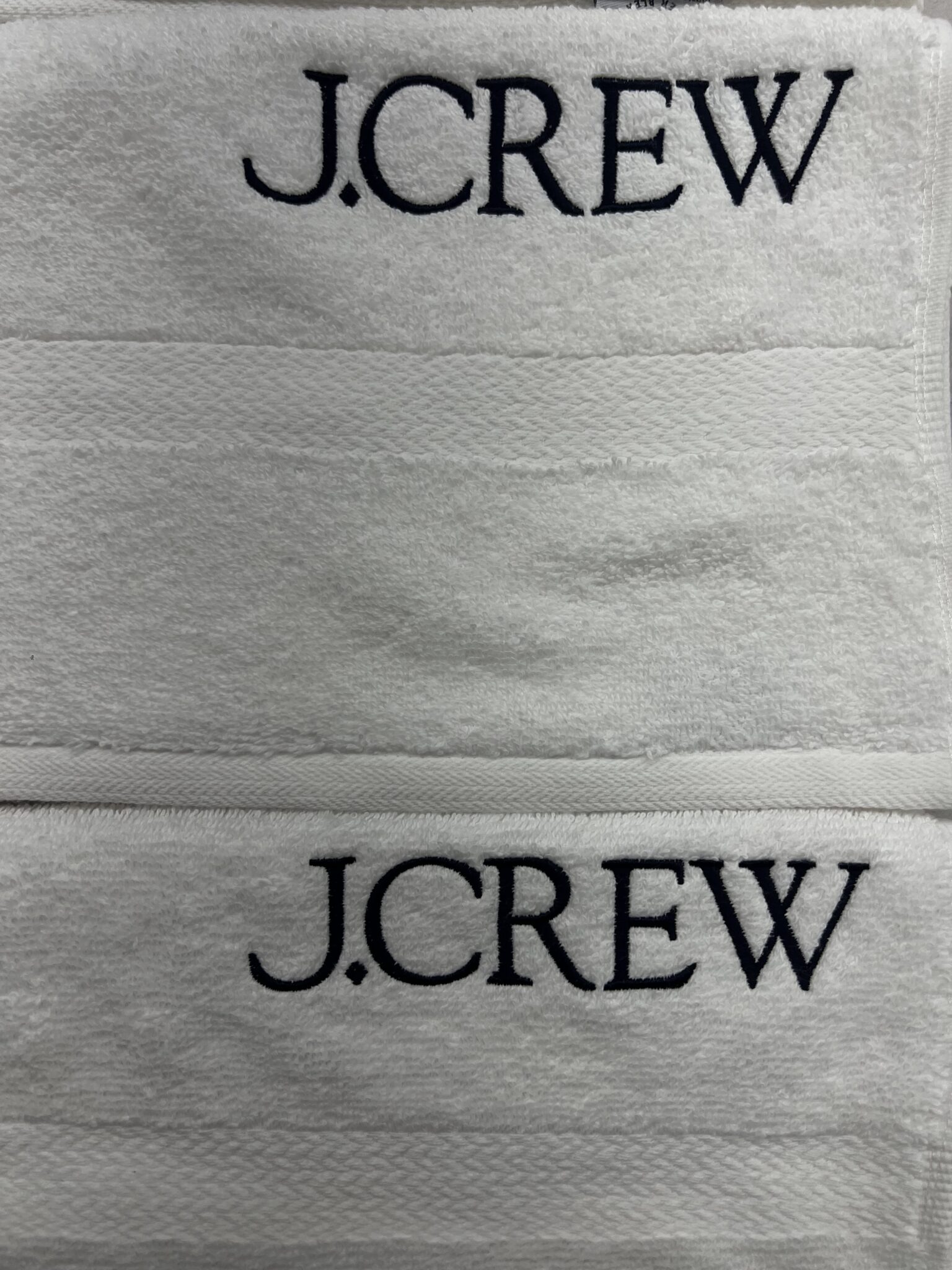 Multiple white towels stacked with embroidered J.Crew logos