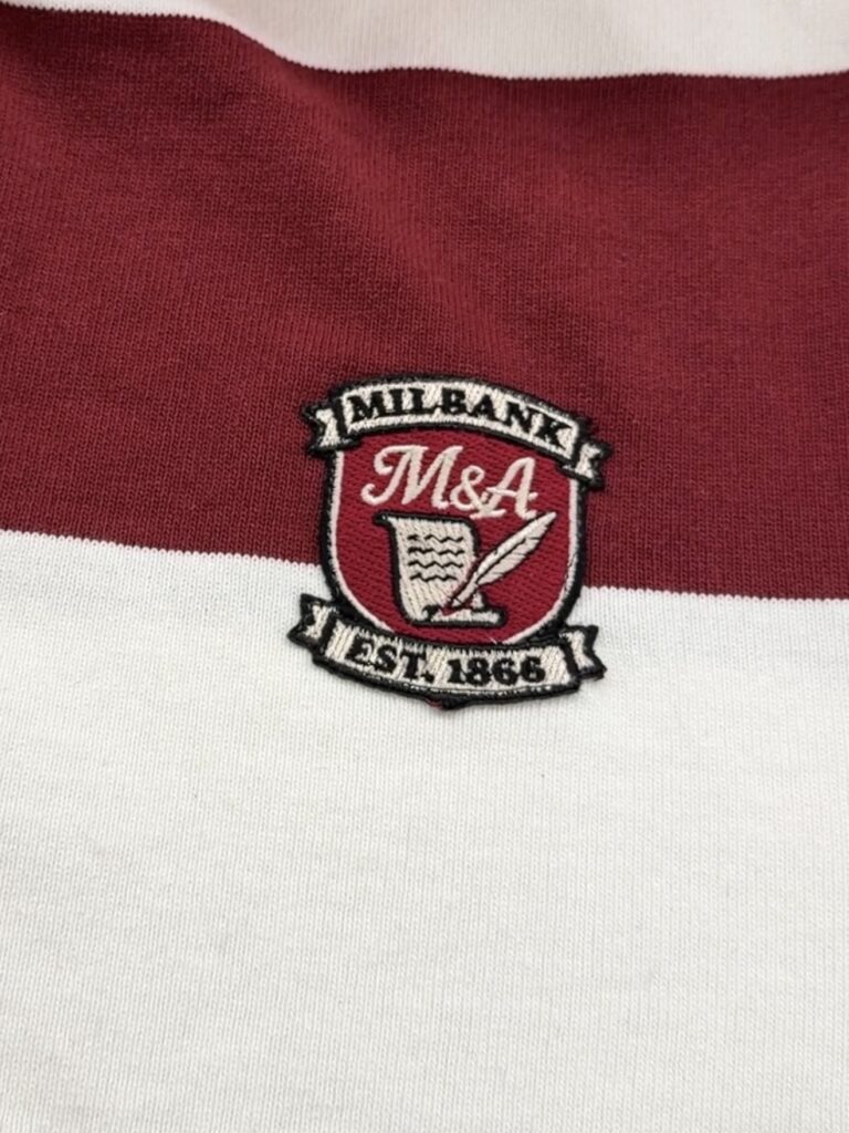 Close-up of embroidered Milbank crest patch stitched onto striped rugby-style garment