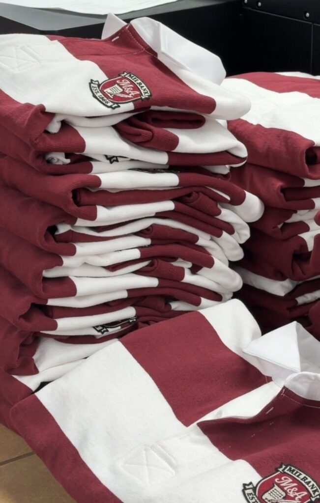 Stack of striped rugby shirts featuring embroidered Milbank crest patches applied in production