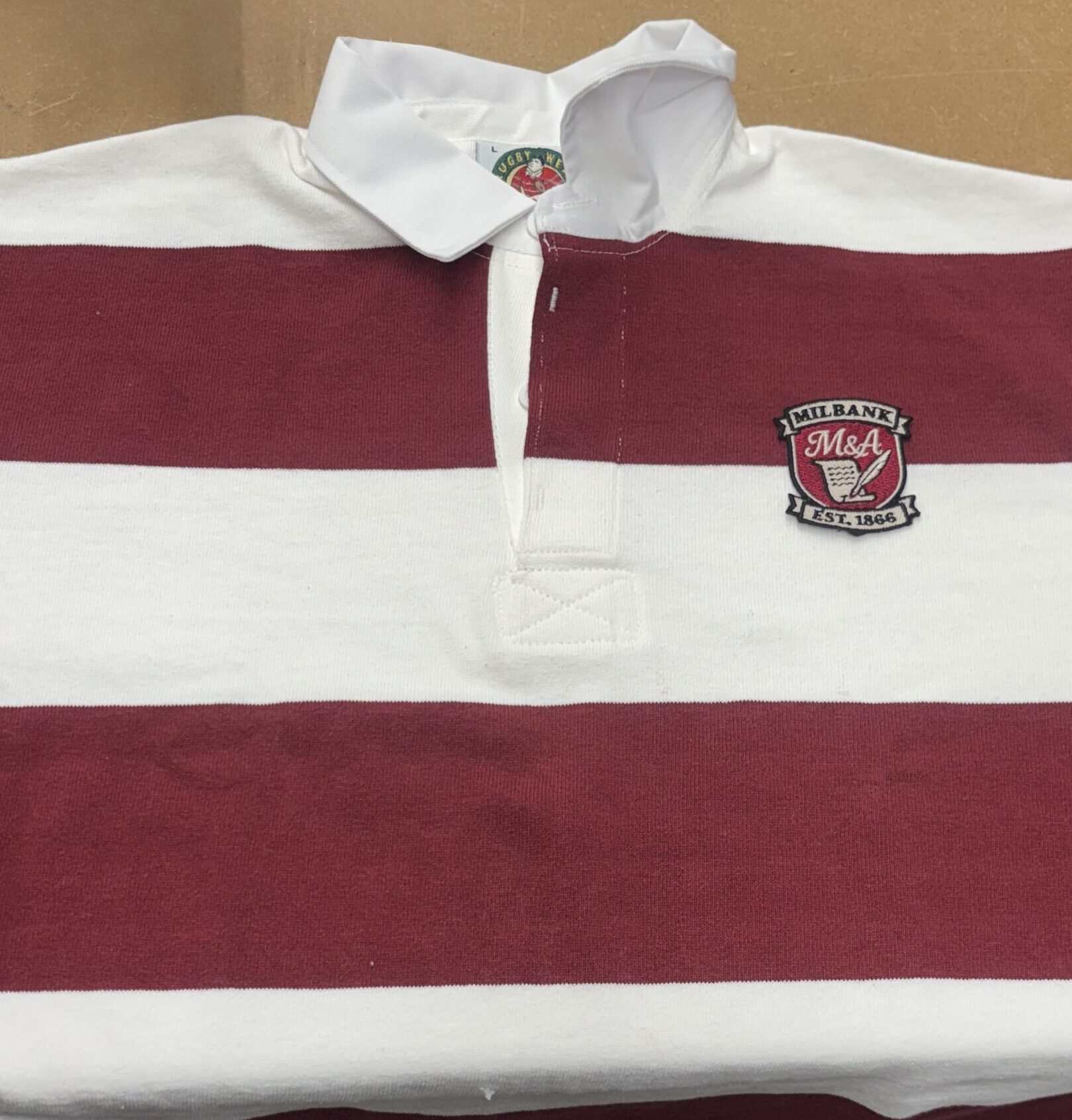 Close-up of embroidered Milbank crest patch stitched onto striped rugby-style garment