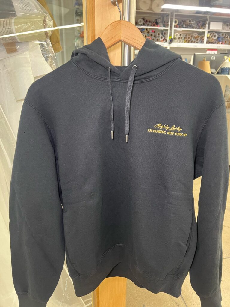 Close-up of Mighty Lucky embroidery stitched in gold thread on a black hoodie