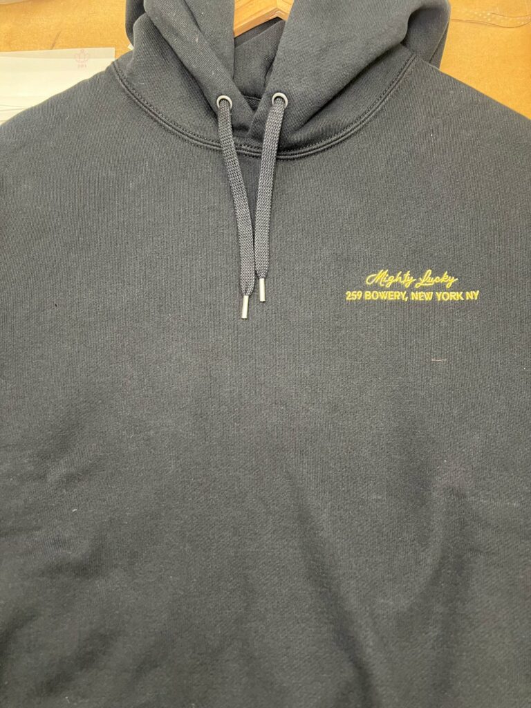 Close-up of Mighty Lucky embroidery stitched in gold thread on a black hoodie