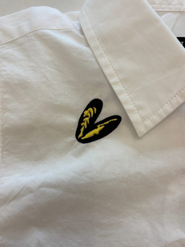 Small embroidered motif stitched onto white J.Crew garment near placket