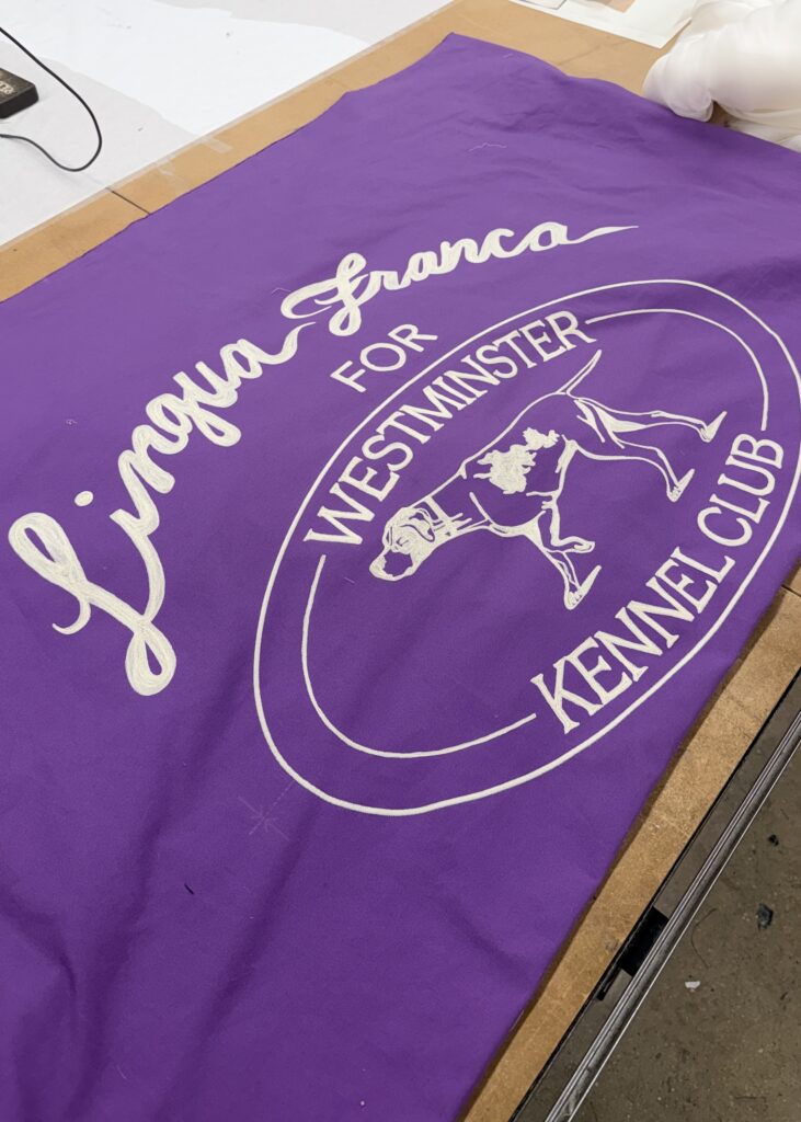 Chain stitch embroidered banner for Lingua Franca featuring white lettering and dog illustration on purple fabric for the Westminster Kennel Club Dog Show