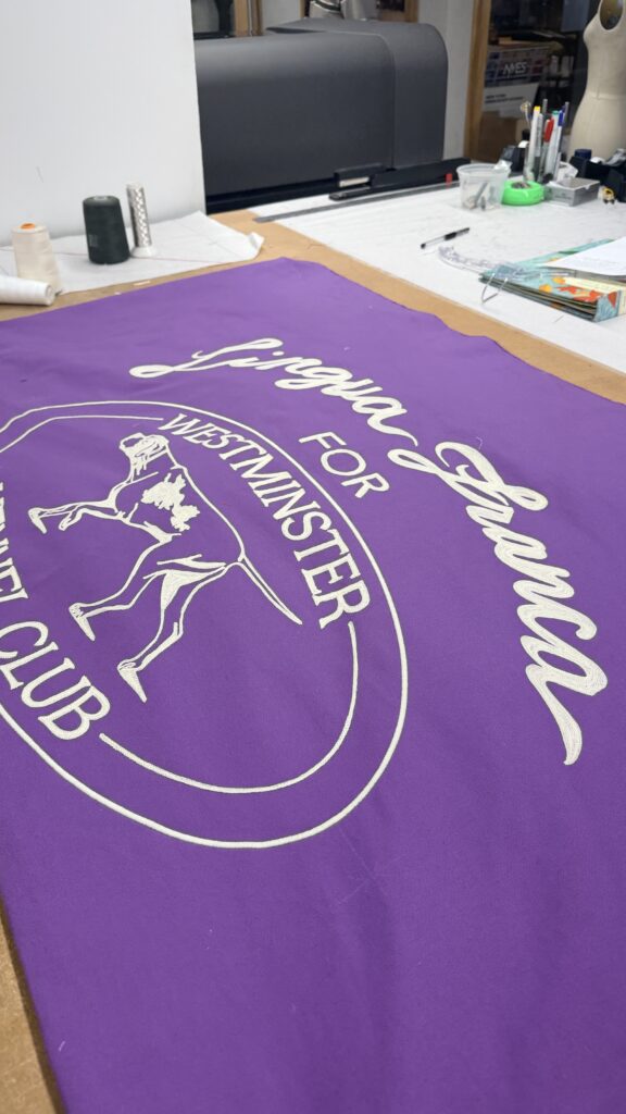 Chain stitch embroidered banner for Lingua Franca featuring white lettering and dog illustration on purple fabric for the Westminster Kennel Club Dog Show