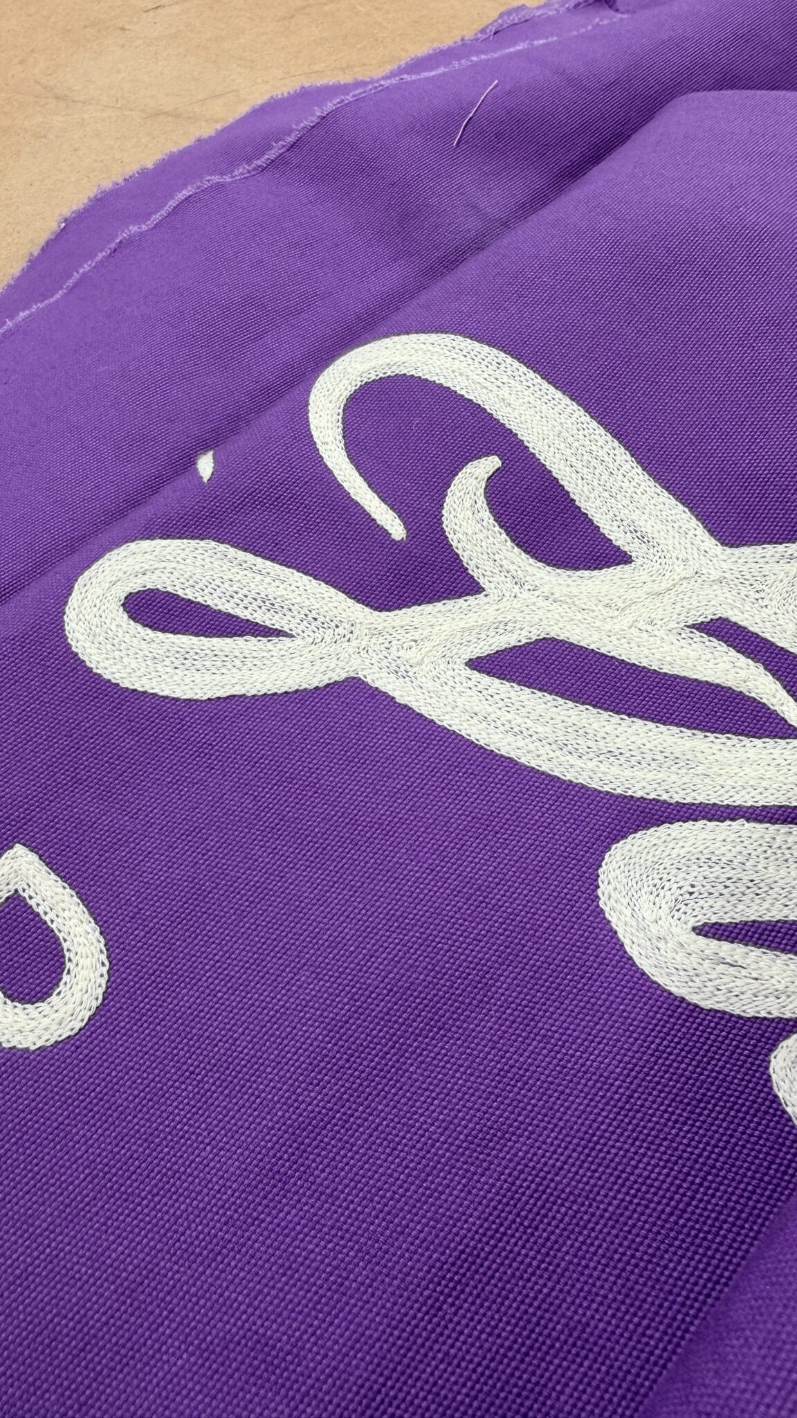 Close-up of white chain stitch embroidery on purple fabric showing detailed lettering for Lingua Franca Westminster Kennel Club banner