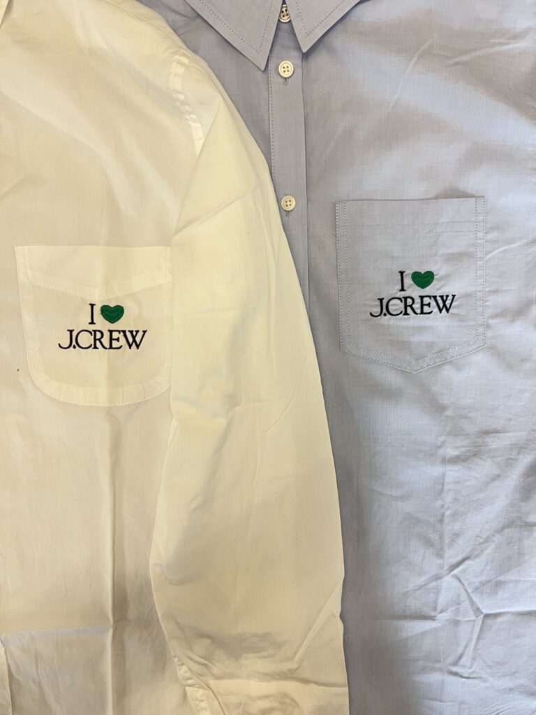 Close-up of embroidered logo positioned above chest pocket on white button-down shirt