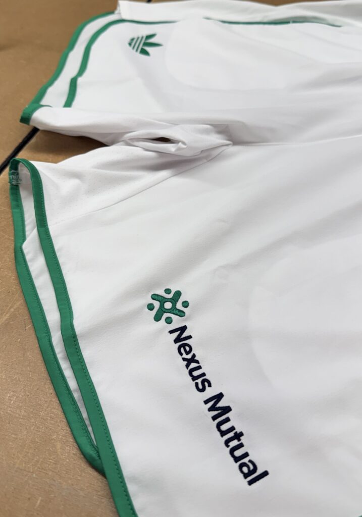 white Adidas performance apparel with green trim and multiple embroidered corporate logos