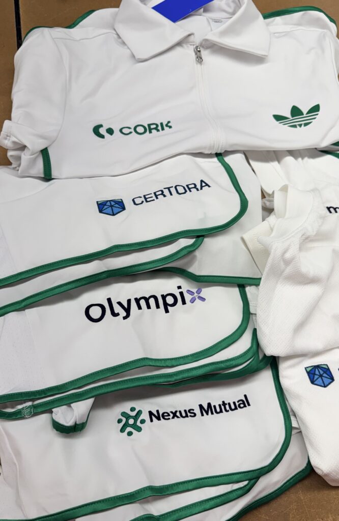 Stacked white Adidas performance apparel with green trim and multiple embroidered corporate logos