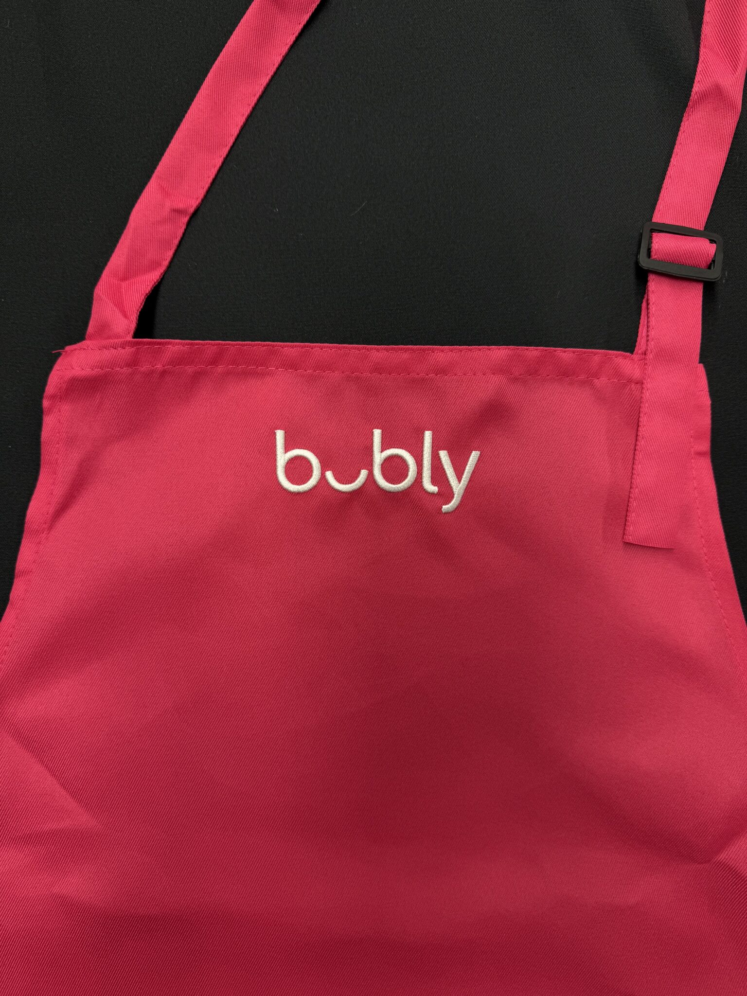 Close-up of pink bar apron with adjustable strap and custom bubly embroidery