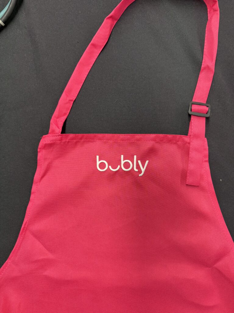 Close-up of pink bar apron with adjustable strap and custom bubly embroidery