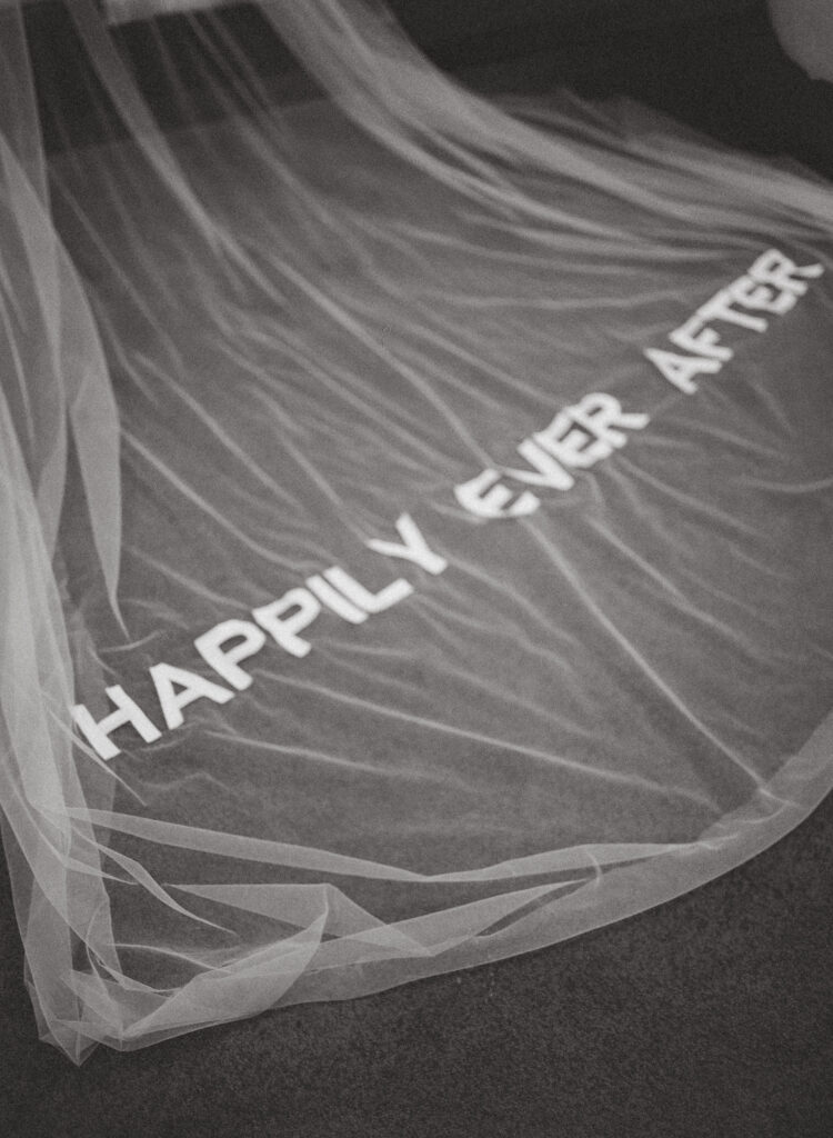 Custom embroidered bridal veil with “Happily Ever After” text laid out in studio workspace