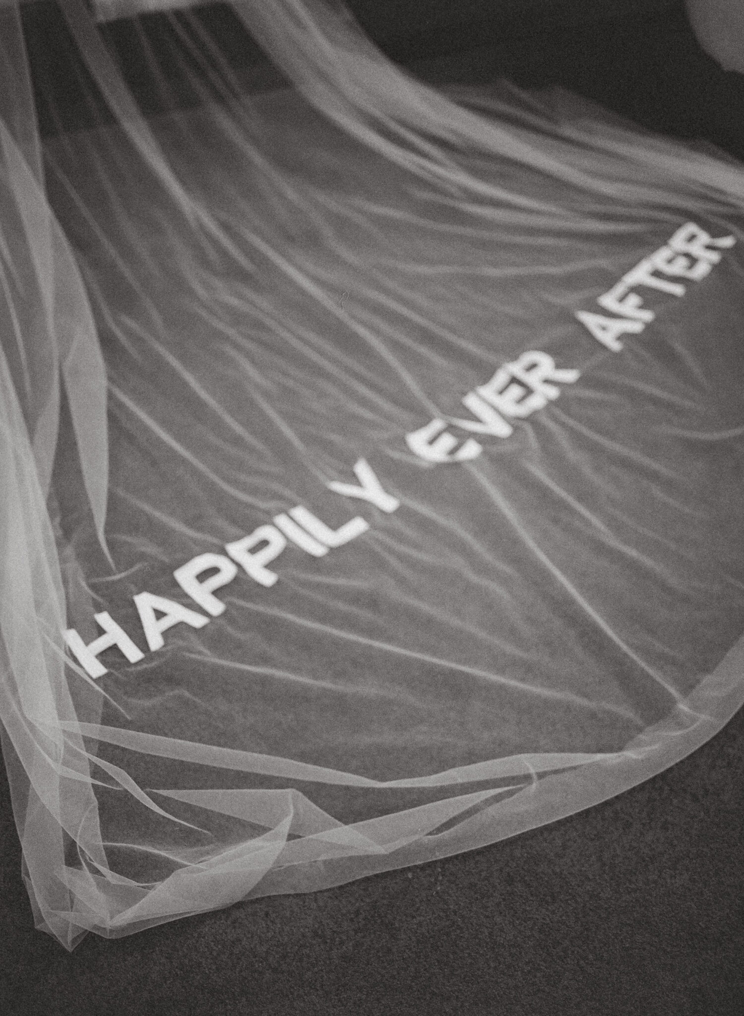 Custom embroidered bridal veil with “Happily Ever After” text laid out in studio workspace