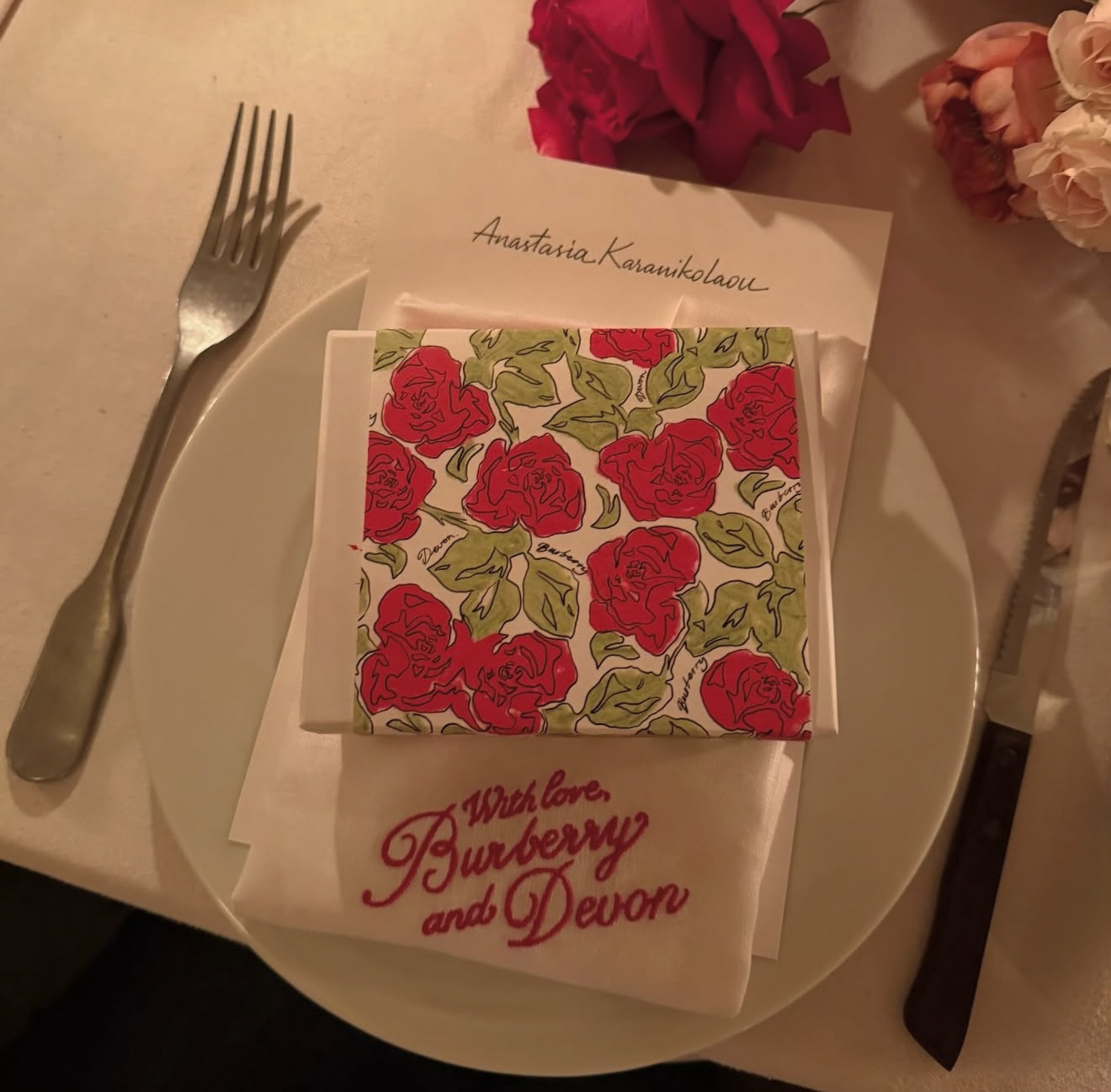 Custom embroidered napkin reading “With Love, Burberry and Devon” at candlelit luxury dinner with rose floral tablescape