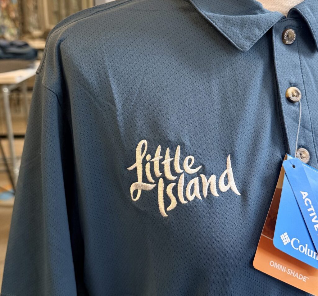 hite embroidered Little Island logo on teal and navy Columbia Sportswear performance uniforms for the brand's staff apparel refresh.