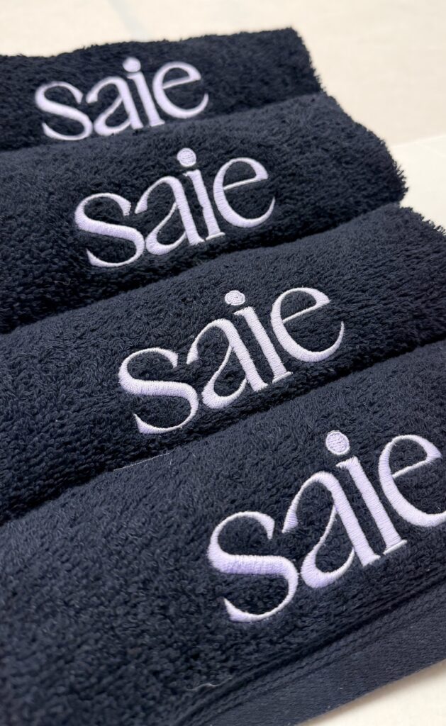 Saie Beauty logo in lavender-white thread on charcoal custom embroidered beauty towels.