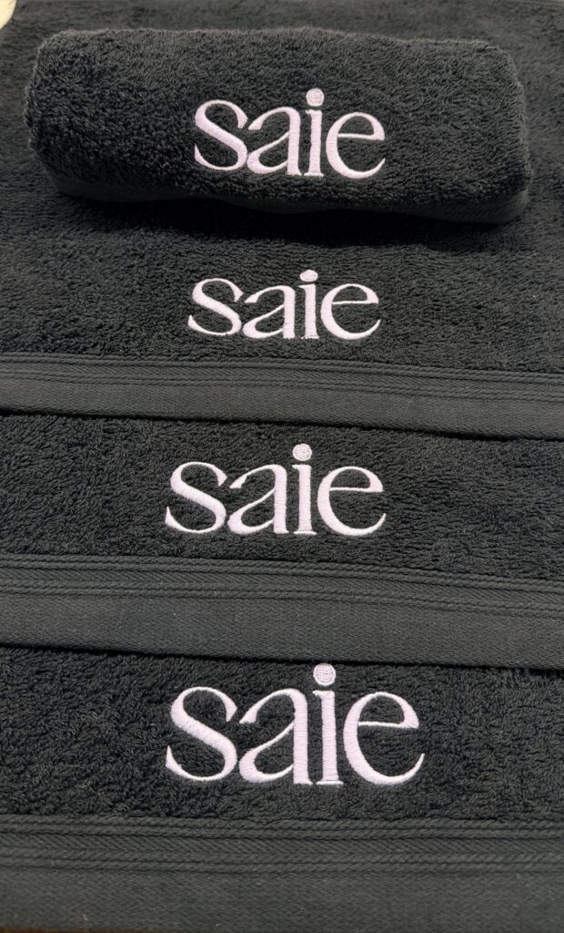 Saie Beauty logo in lavender-white thread on charcoal custom embroidered beauty towels.
