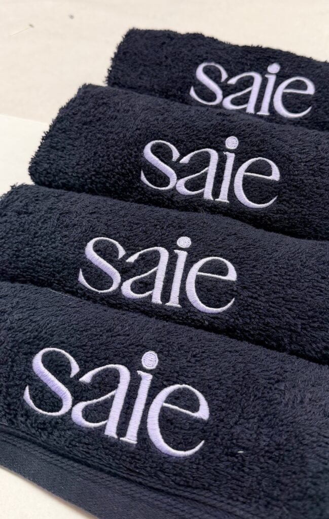 Saie Beauty logo in lavender-white thread on charcoal custom embroidered beauty towels.