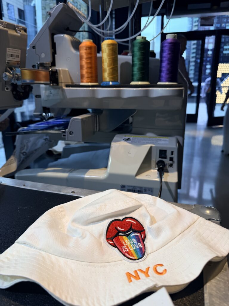 Live embroidery and heat press customization station creating personalized Pride bucket hats and bandanas during the One Times Square Pride celebration.
